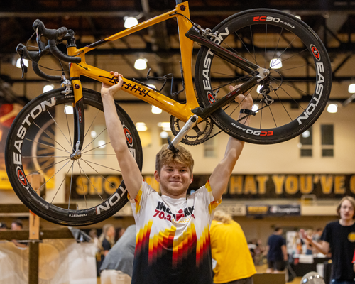 Student holding bicycle at event.